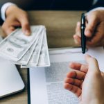 A person cautiously assessing a stack of money with a pen, symbolizing potential red flags when applying for a personal loan