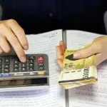 A person holding a calculator and a stack of money to calculate payday loansin Colorado