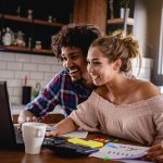 Young couple planning a home budget sitting at a table looking at a laptop