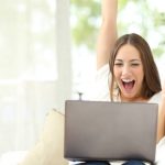 Excited girl celebrating good news on laptop sitting on a couch at home