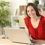 Happy woman with laptop gesturing thumbs up at home