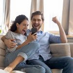 Excited couple on couch celebrating approval of their "No Credit Check & Bad Credit" payday loan in North Dakota on their phone.