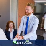 A man shaking hands with a woman in a white shirt and blue tie after finding out how long they have to wait to get another payday loan