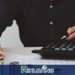 A man sitting at a table with a calculator and a stack of coins trying to find out the difference between a payday loan and a tribal loan