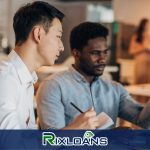 Two men sitting at a table in front of a laptop computer discussing payday loans in Dallas