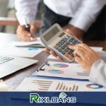 A person holding a calculator in front of a laptop working on installment loans charts in New York